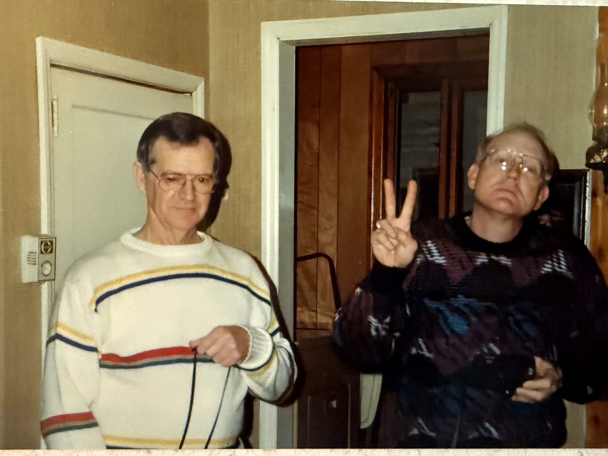 Two people indoors, one giving a peace sign, from a digitized print